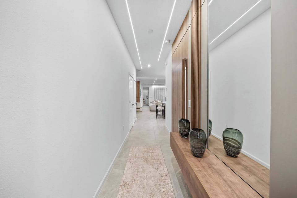 Step into a beautifully designed hallway with sleek white walls and warm wooden accents that invite you in. The soft glow of recessed lighting highlights the stylish decor, complemented by elegant vases for a sophisticated touch.