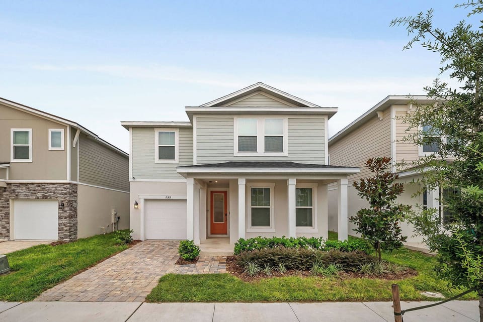 Step into a charming façade featuring a classic front porch framed by lush greenery, inviting you to relax and unwind. The light-colored siding and clean lines create a welcoming ambiance, perfect for your next vacation.