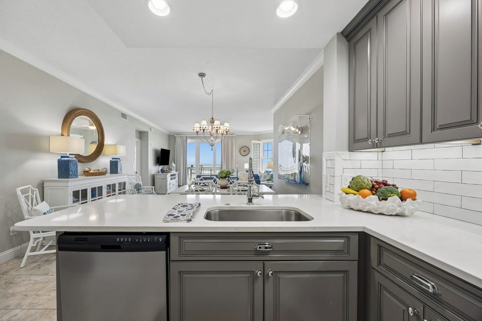 Your open kitchen features elegant gray cabinetry, white quartz counters, and stainless appliances—perfect for preparing meals while staying connected to family and ocean views beyond.