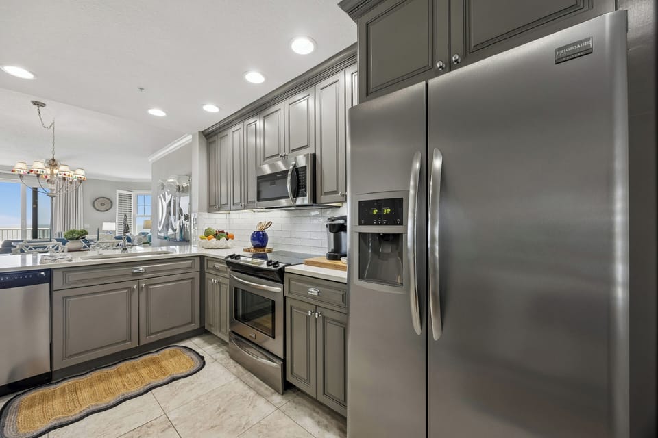 Prepare your favorite meals in this fully equipped kitchen featuring sleek stainless steel appliances, elegant gray cabinetry, and gleaming white subway tile backsplash that catches the warm natural light.
