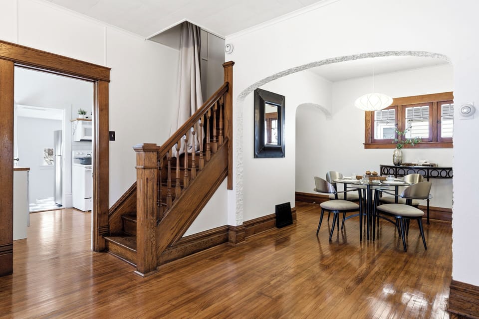 Spacious dining area with polished hardwood floors, original wood staircase, arched entryways, and warm historic charm.
