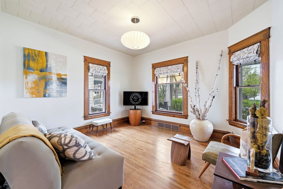 Bright, inviting living room with warm wood trim, hardwood floors, modern decor, and large windows that fill the space with natural light.