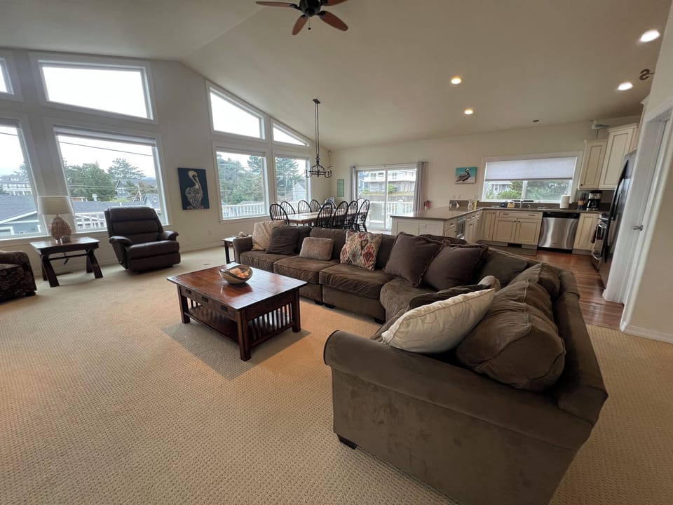 Relax in your spacious, sunlit living area featuring plush seating, a dining table, and a fully equipped kitchen—all bathed in natural light from oversized windows.