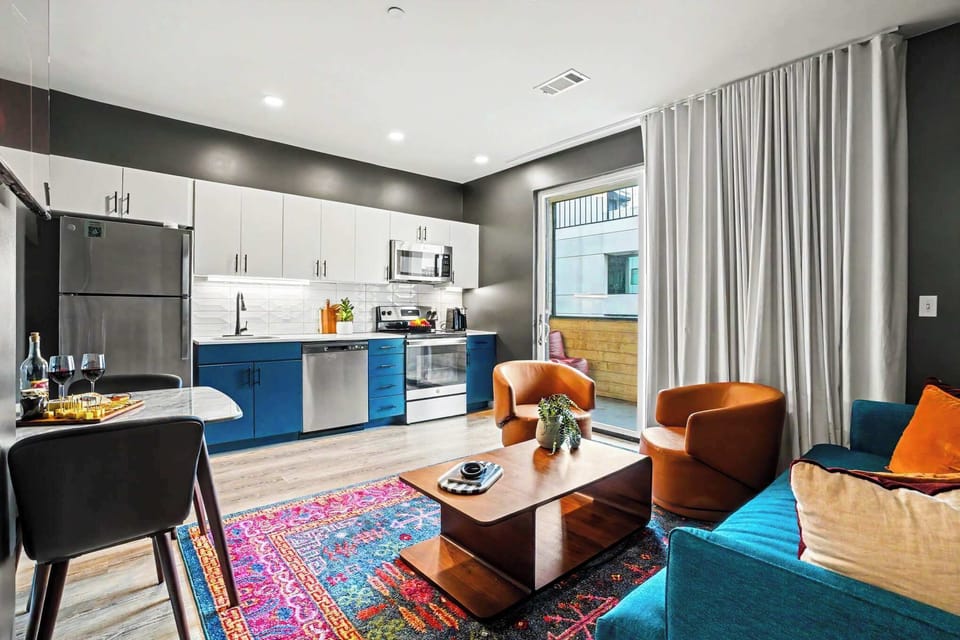 The living area brings bold personality with a teal sofa, leather swivel chairs, a sculptural wood coffee table, vibrant area rug, music-inspired art and a large smart TV.