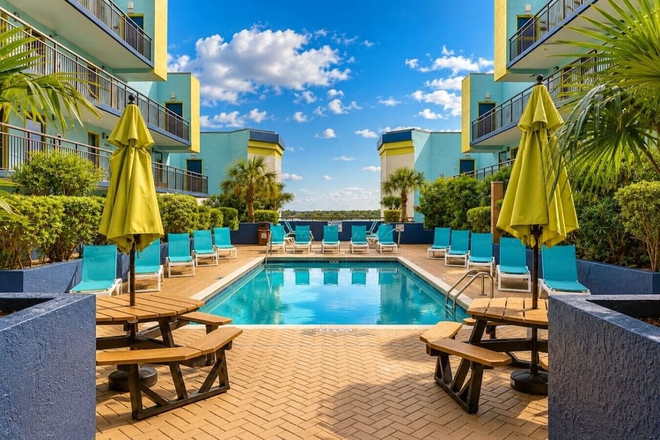 Take a dip in paradise. This sun-drenched pool is surrounded by lounge chairs, tropical greenery, and colorful buildings that give the space a resort-like feel. With picnic tables under yellow umbrellas and palm trees swaying overhead, it`s the perfect sp