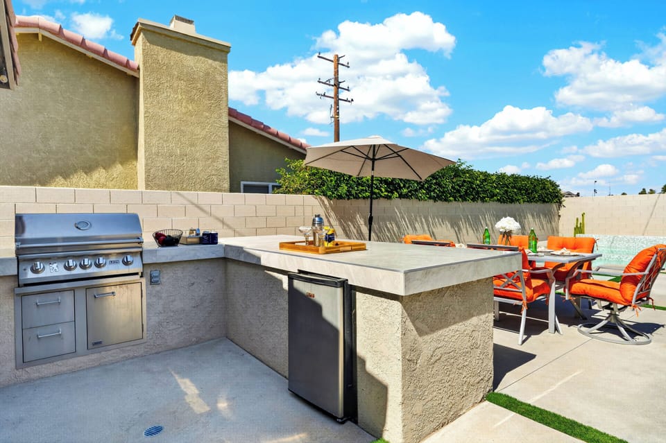 Outdoor entertainer's kitchen equipped with a built-in stainless steel grill, ample counter space, and a mini-fridge.