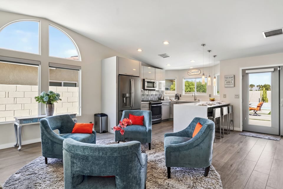 Sun-drenched conversational lounge featuring plush teal velvet armchairs arranged beneath a grand architectural arched window.