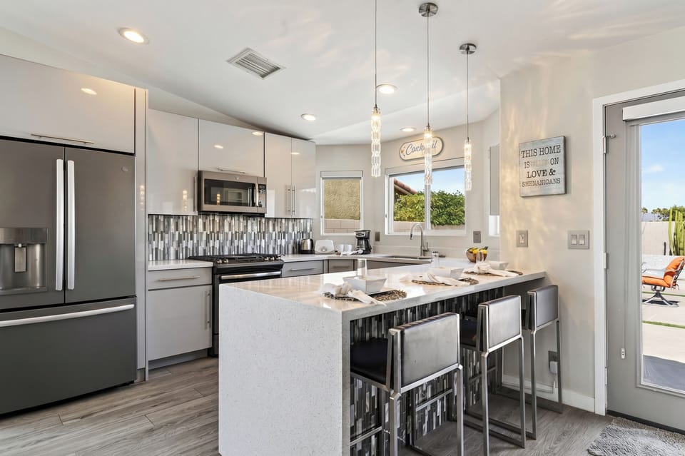 Chef’s kitchen complete with minimalist white cabinetry, stainless steel appliances, and a massive waterfall-edge island with bar seating.