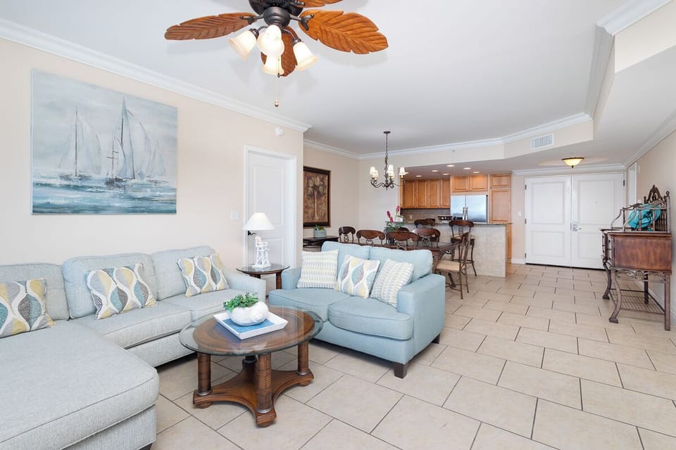 Relax into coastal comfort in this open-concept living space where soft blues meet warm wood tones. A tropical ceiling fan keeps you cool while you unwind on plush seating before exploring your fully equipped kitchen.
