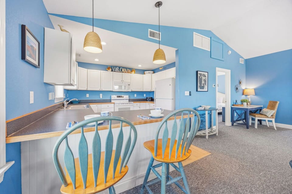 Settle into your bright, beachy kitchen with coastal-blue walls, white cabinetry, and charming woven pendant lights—perfect for morning coffee at the breakfast bar or preparing meals together.