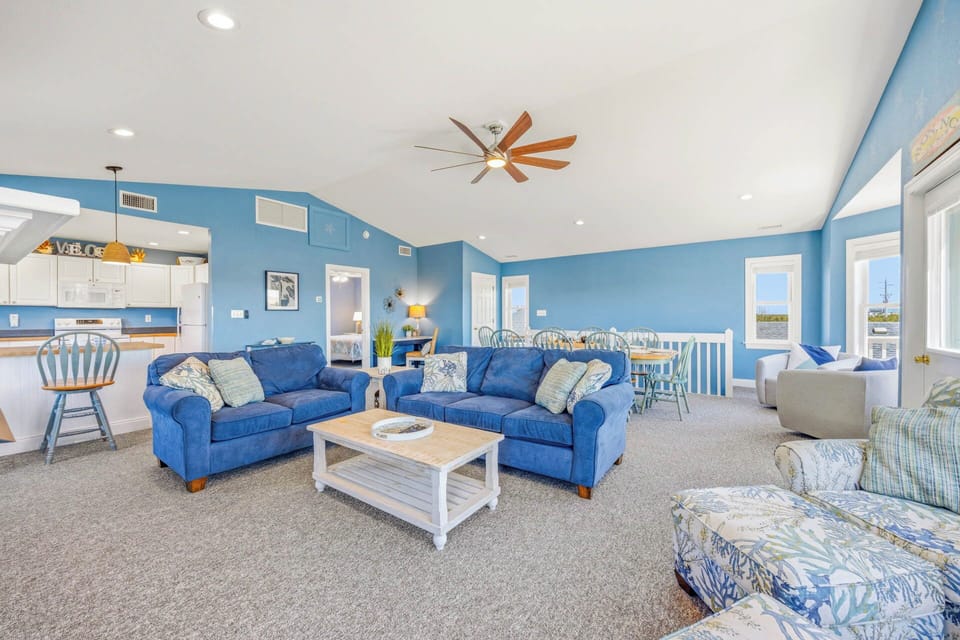 Relax into coastal comfort in your spacious living room, where plush blue sofas, cheerful accents, and abundant natural light create the perfect beach retreat for your group.