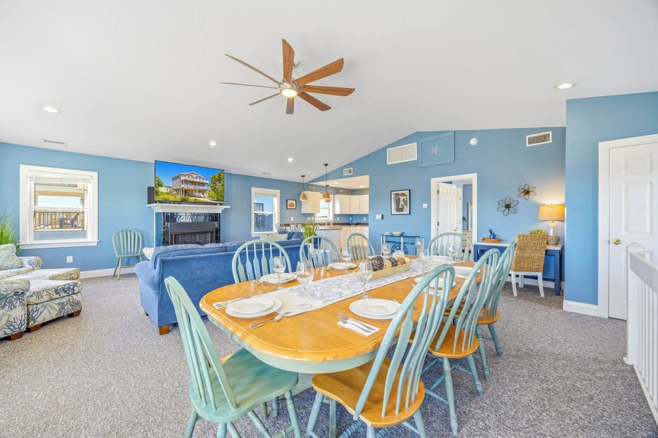 Gather around the cheerful dining table while ocean breezes swirl from the ceiling fan above. This open, airy space invites laughter and connection, with coastal-blue walls and sunlit views framing your perfect vacation meals.