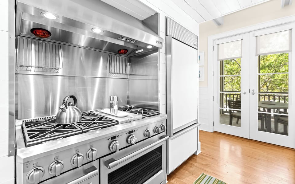Your chef-ready kitchen features a professional gas range and gleaming stainless steel exhaust, with balcony doors opening to serene tree-lined views.