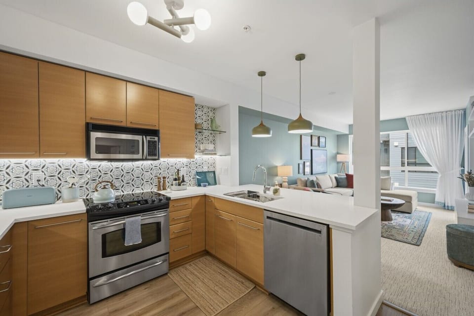Fully equipped modern kitchen with stainless steel appliances, spacious countertops, bar seating, pendant lighting, cookware, and everything needed for cooking meals at home.