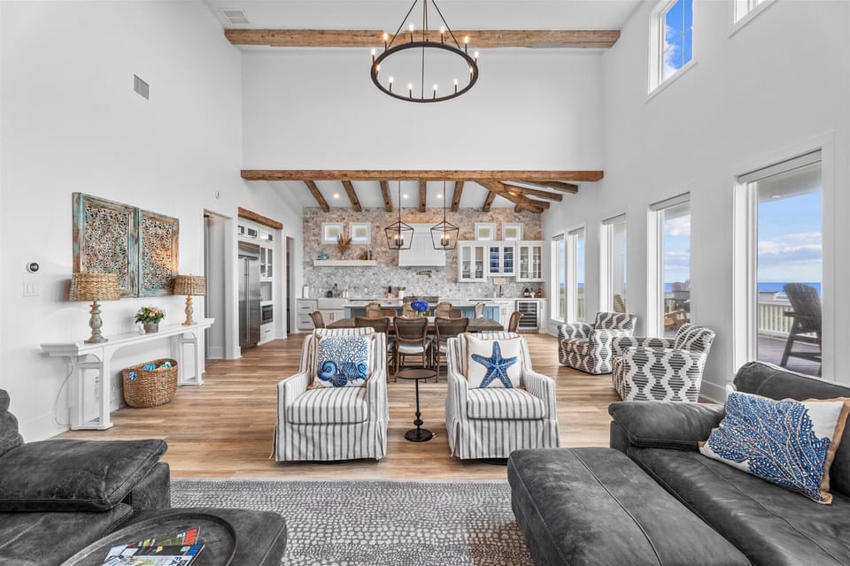 Coastal-inspired great room with vaulted ceilings, modern furnishings, exposed beams, and seamless flow into kitchen and dining areas.