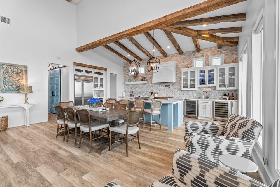Spacious dining and living area with exposed wood beams, large windows, and elegant coastal décor throughout the vacation home.