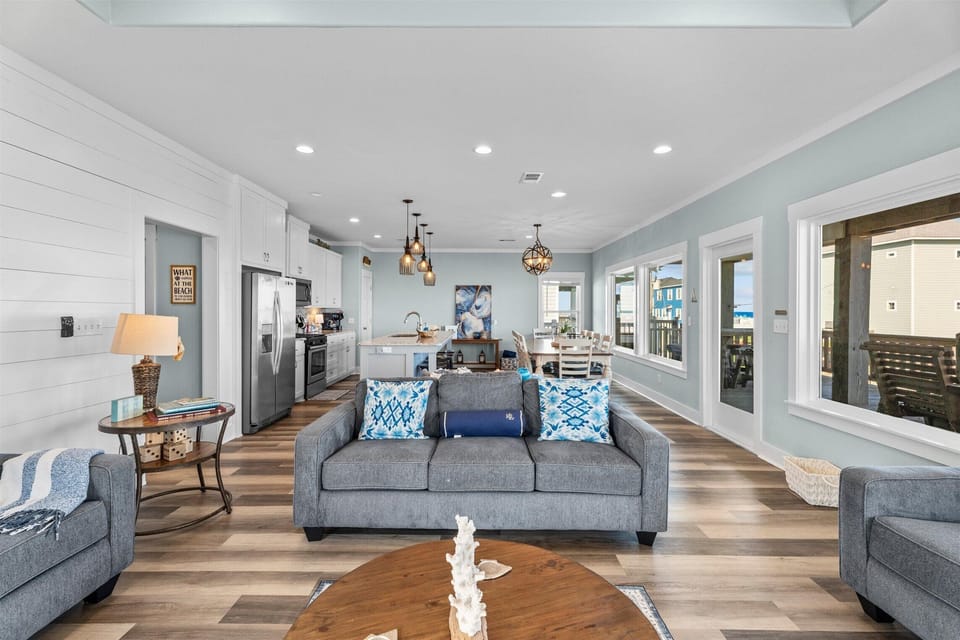 Elegant open living space with oversized sectional sofa, coastal furnishings, and seamless access to dining and kitchen areas for group gatherings.