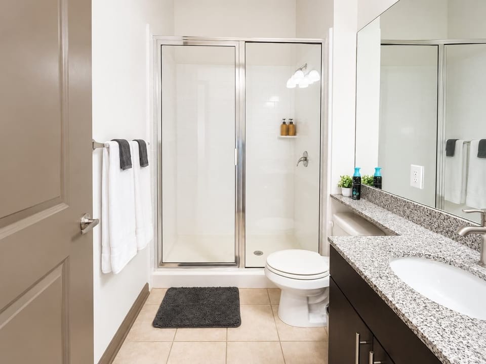 Clean bathroom with a glass-enclosed shower, granite vanity, bright lighting, and fresh white finishes.