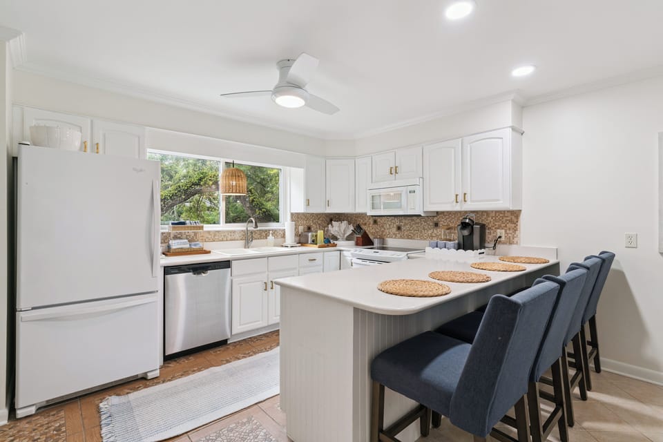 Gather around the bright kitchen island with modern appliances and a garden view. Thoughtful details like the ceiling fan and breakfast bar seating create a welcoming space for your morning meals.