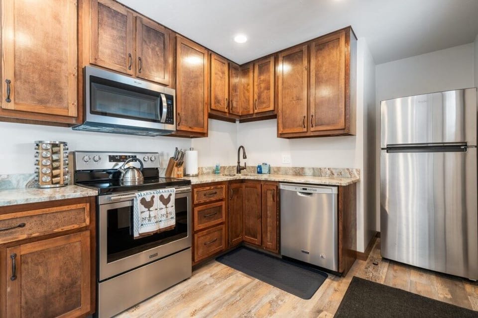 Kitchen with stainless steel appliances, wood cabinets, marble countertops.
