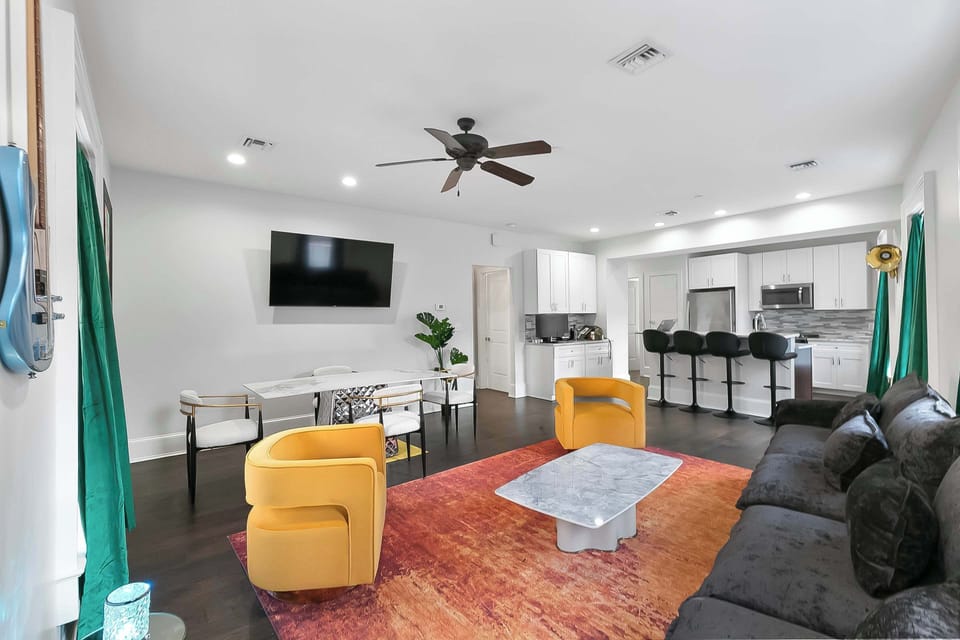 Bright living room with a huge sofa and adjoining cozy dining area perfect for meals and gatherings. Gallery walls by Ayodele Owolabi, real instruments that softly light up at night, smart TV, and easy access to Magazine Street.