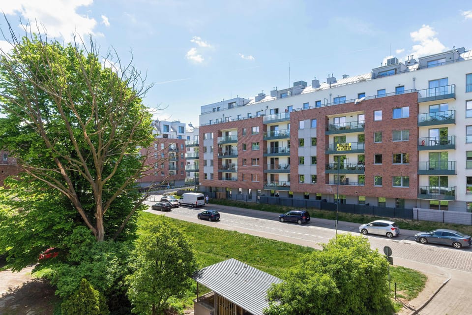 A green outdoor area overlooking residential apartment buildings and landscaped surroundings. Trees and shrubs add a peaceful touch to the urban scenery.