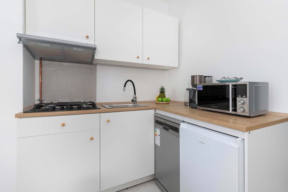 A minimalist kitchenette with white cabinets, wooden countertops, and modern appliances. Clean lines and neutral colors give the space a contemporary feel.