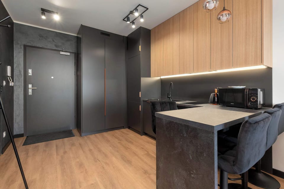 A low-angle view facing the kitchen and entryway emphasizes the aesthetic appeal of the wood-look floor planks. The dark furniture fronts blend cohesively with the graphite-toned walls of the corridor.