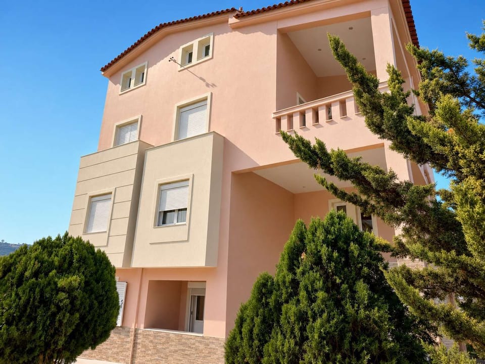 Exterior facade of the building with landscaped surroundings, offering a peaceful residential atmosphere near beaches, tavernas, and ferry connections.
