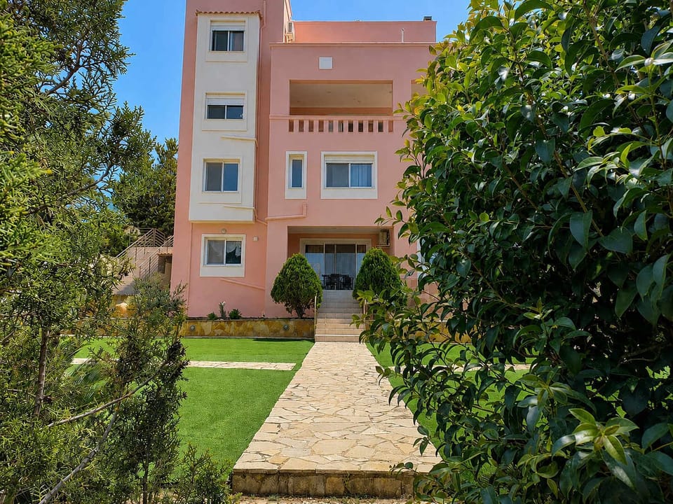 Exterior view of the building surrounded by greenery and shared outdoor spaces, located in a quiet residential area close to Salamina Marina and Paloukia Port.