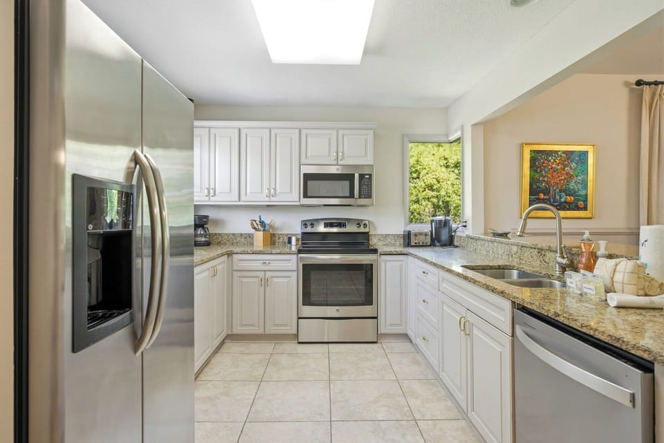 Gleaming stainless steel appliances pair with speckled granite counters in this airy, functional kitchen. White cabinetry and garden views create a cheerful workspace for brewing your morning coffee or preparing a shared meal.