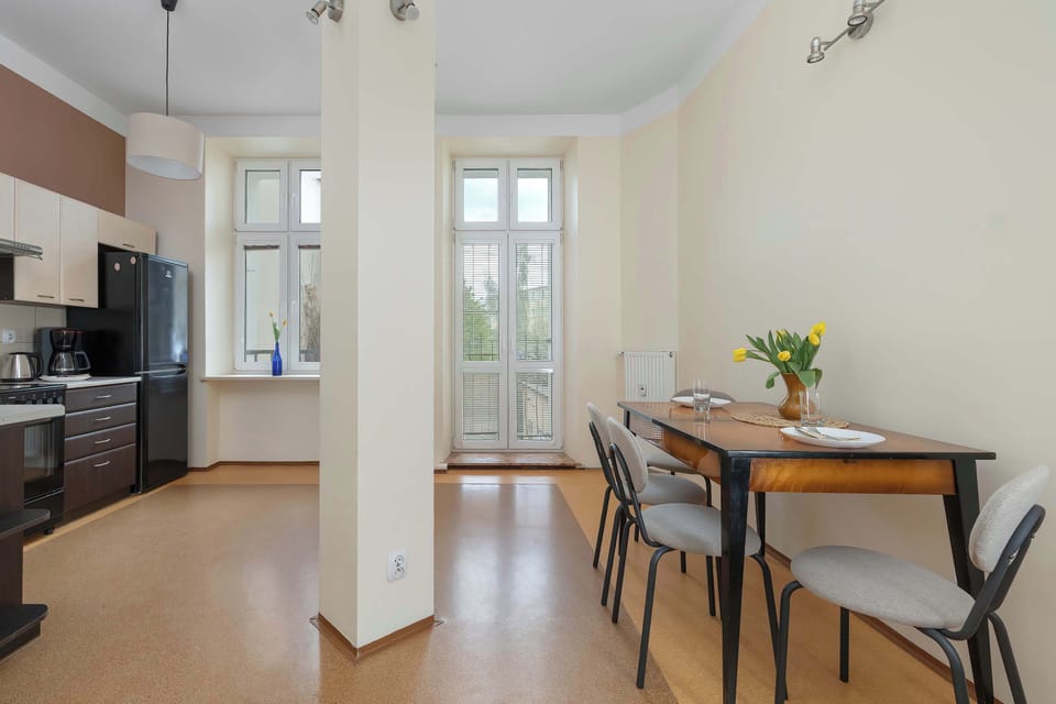 A large open-plan kitchen and dining space with modern cabinetry and a wooden dining table. Wide windows and white columns give the room a spacious feel.