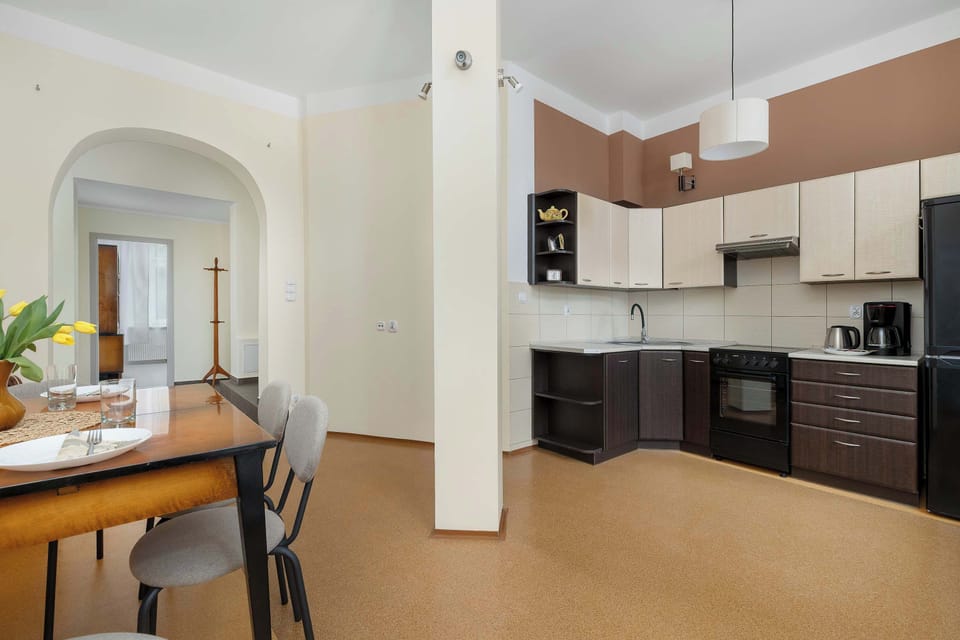 A bright dining area adjacent to the kitchen, furnished with a wooden table and upholstered chairs. Natural light enters through balcony doors at the far end.