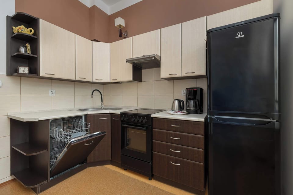 A contemporary kitchen with black and cream cabinets, integrated appliances, and tiled flooring. The layout offers generous preparation space and modern finishes.