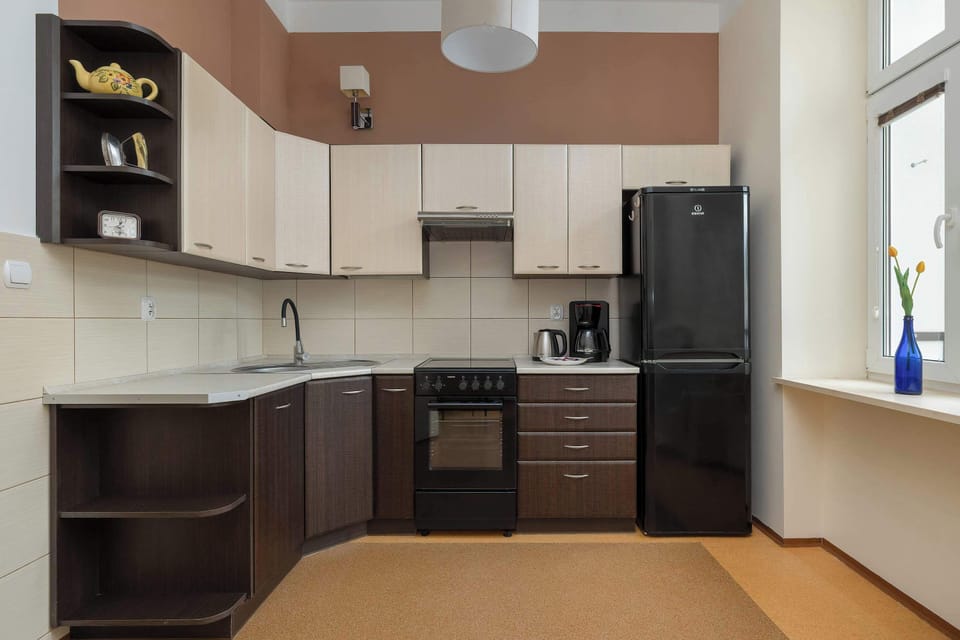 A spacious kitchen equipped with dark lower cabinets, cream upper cupboards, and modern appliances. Large windows brighten the room and highlight the clean countertops.