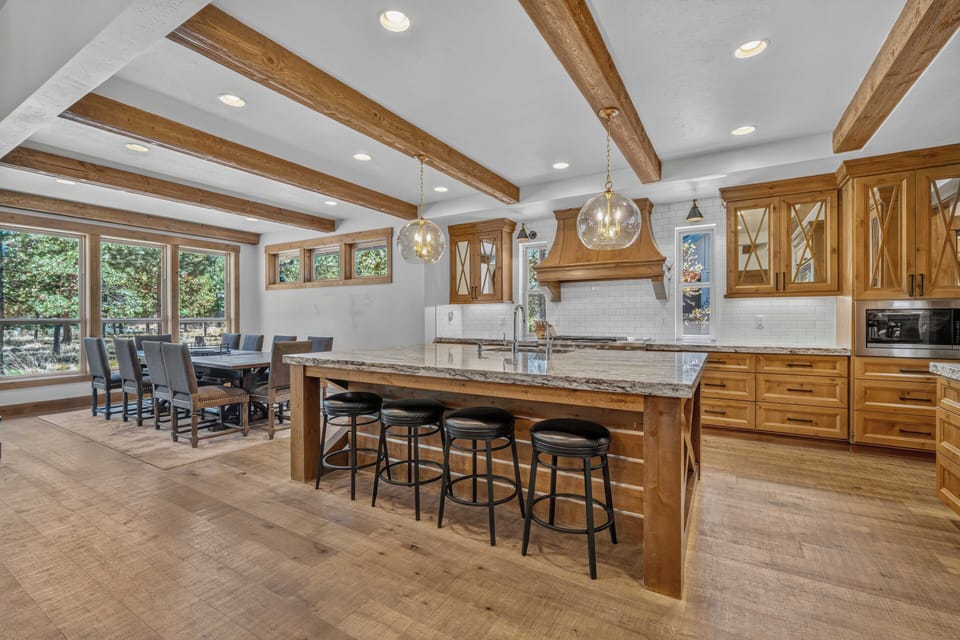 Gather around the spacious kitchen island or enjoy meals at the farmhouse dining table, all beneath charming exposed beam ceilings with views of the surrounding greenery.