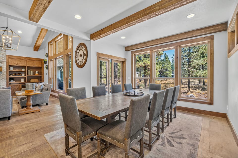 Gather around this handsome dining table beneath rustic wood beams, with sunlight streaming through tall windows. Your group will love sharing meals here with forest views all around.