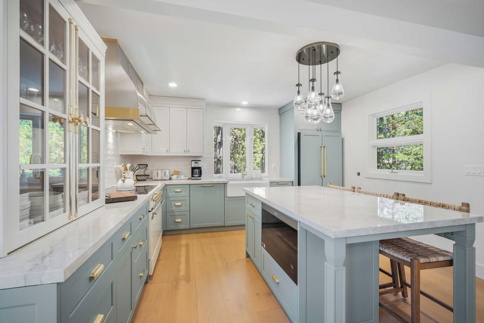 Step into your beautifully designed kitchen, where soft blue cabinetry, elegant marble countertops, and modern pendant lighting create the perfect space for cooking and gathering together.