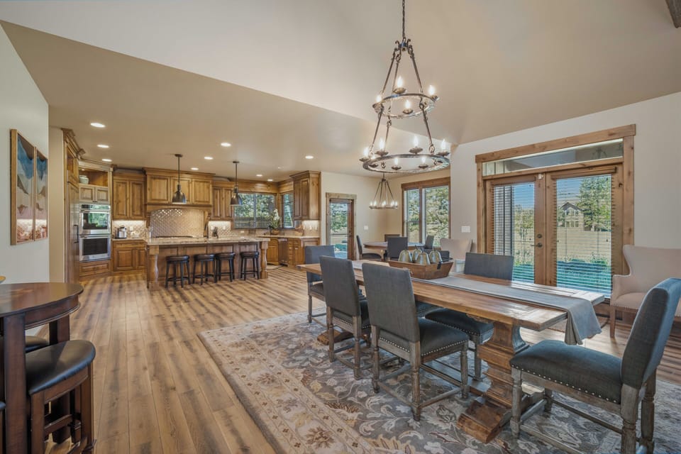 Gather around a handsome wood dining table where meals become moments. Natural light pours through grand windows revealing scenic views, while the open kitchen beckons with rich cabinetry and an inviting island—your home away from home.