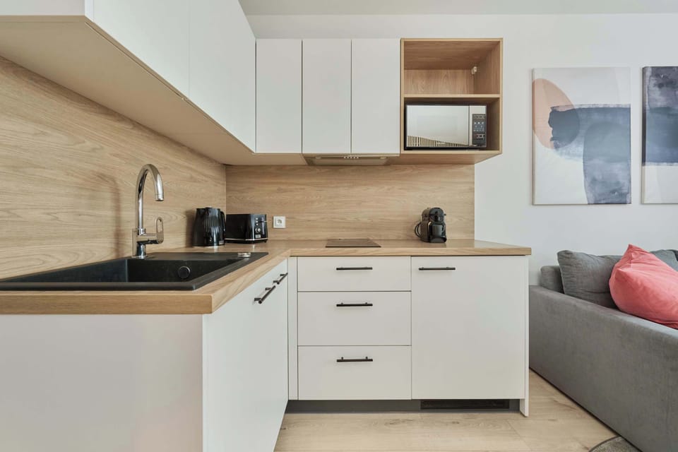 A modern kitchen with white cabinetry, wooden countertops, and compact appliances.

