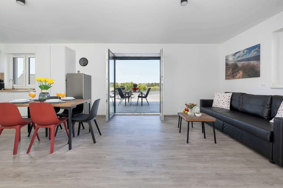 A spacious open-plan interior with a dining table, sofa, and terrace access. The room has a clean and modern design.