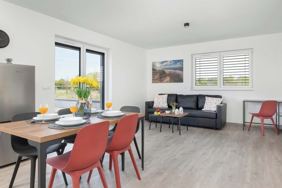 A modern dining area connected to a bright living room. Large windows bring in plenty of natural light.