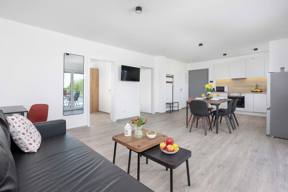 A cozy living room with a sofa, coffee table, and open kitchen area. The apartment looks bright and comfortable.