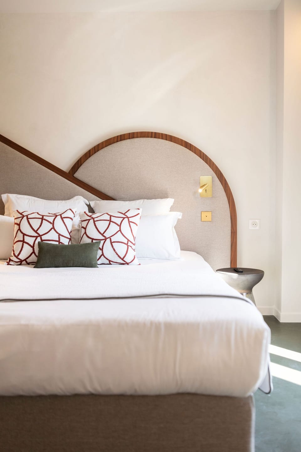 Queen bed with a smooth wooden headboard, decorative pillows, and a metallic bedside stool