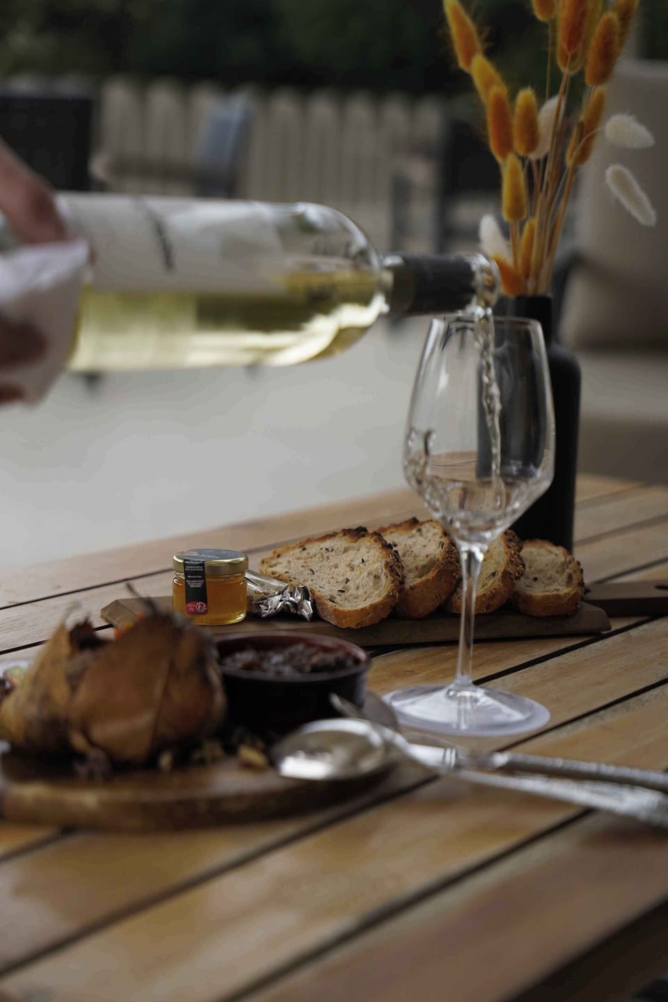 Wine glass and a rustic wooden table setting — looks like an outdoor dining scene with a bottle in background