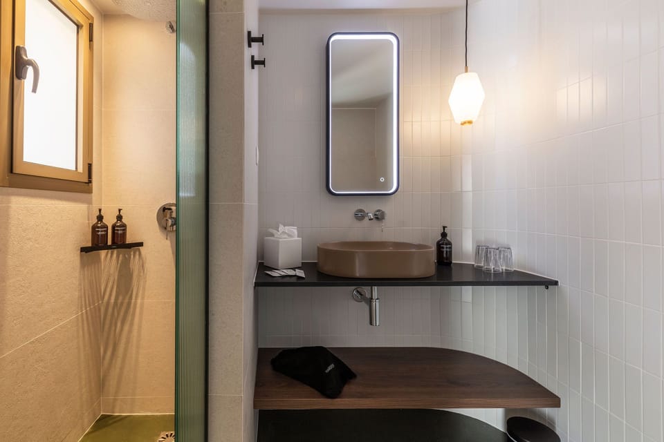 Glass shower, round brown sink on a black countertop, and a backlit mirror in the en-suite