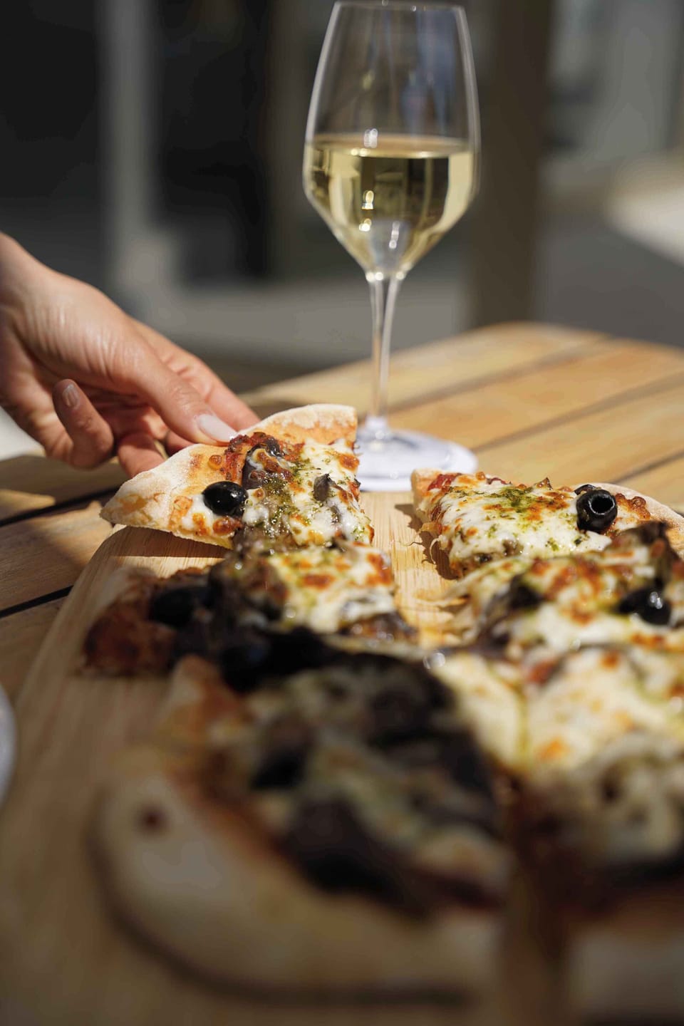 Sharing a pizza on a wooden board with a glass of white wine alongside