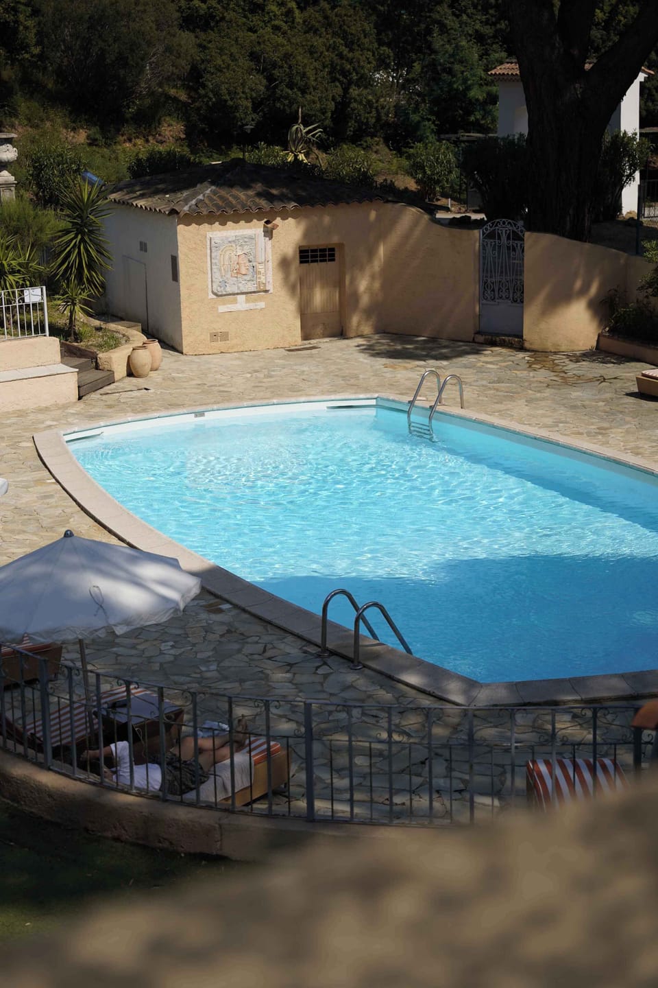 Elevated view of the stone-paved pool terrace, sheltered on all sides by tall green hedges