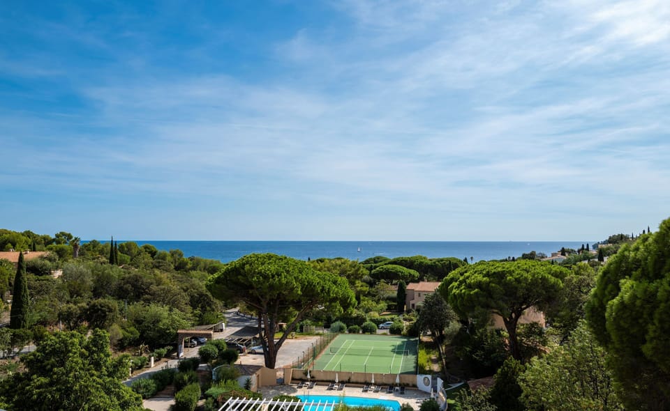 Balcony view across the park — tennis court below and the sea visible on the horizon