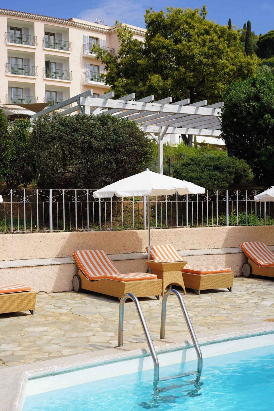 Orange-cushioned wicker loungers line the heated pool — the beach is just a 5-minute walk from here